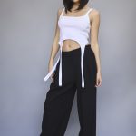 Model with shoulder-length dark hair wearing a white crop top and black wide-leg pants.